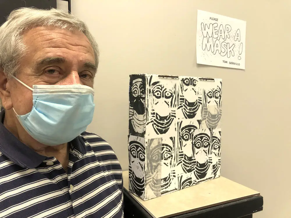 Artist Tom Gargiulo, cofounder of the Gargiulo Arts Foundation, stands beside his multimedia installation “Wear a Mask!” at the Flagler County Art League. Gargiulo will present a talk Saturday, Sept. 19, at the venue. (© FlaglerLive)