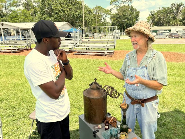 Charlie Cracker, right, details the ways of making “low-bush lightning” to Kalan Lake at Bunnell History Day. FlaglerLive photo