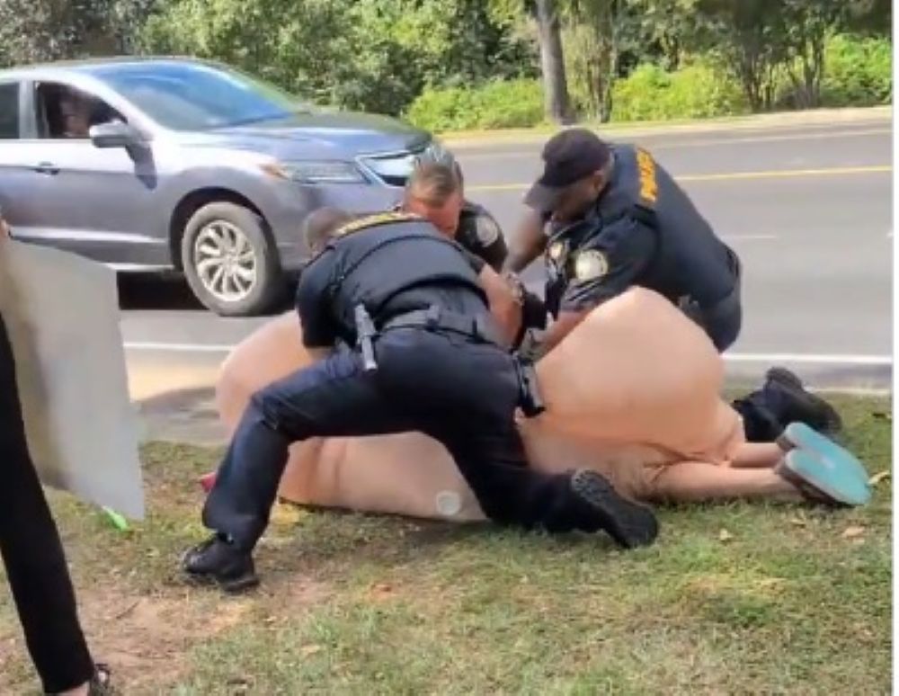 Fairhope police officers arrest a woman dressed in a penis costume in Fairhope, Alabama, on Oct. 18, 2025, during a local “No Kings” protest. Police said Jeana Renea Gamble, 61, was charged with resisting arrest and disorderly conduct, both misdemeanors. Video of the arrest led to widespread criticism of the officers for their actions. (Screenshot via BlueSky)
