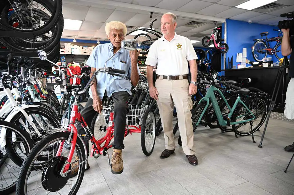Francisco Diaz, who turns 80 next month, is back on a brand new bike after his porevious bike was totaled in a crash with a car on State Road 100, when Sheriff Rick Staly, right, responded, and helped organize a fund-raiser to get Diaz back on his wheels. (© FlaglerLive)