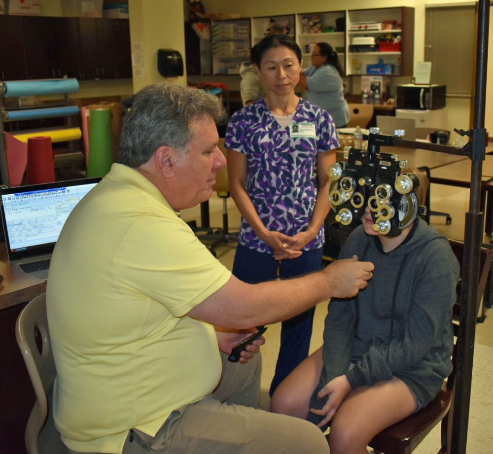 RN & School Health Coordinator Stephanie Ear looks on as an optometrist from Florida Heiken screens a student.