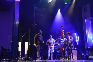 Jonathan Fisk, cello, performing with Black Violin's Kev Marcus during a master class Black Violin held with the Harmony Orchestra on Dec. 3 at the Flagler Auditorium. The FYO's Brooklyn Hoffman is standing by to play. Click on the image for larger view. (© FlaglerLive)