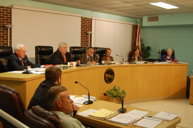 Bruce Campbell, in the foreground, is still the executive-in-waiting as the Flagler Beach City Commission ponders his fate. Drew Smith, the city's attorney, is sitting next to Campbell. On the dais, from left: Marshall Shupe, Steve Settle, John Feind, Jane Mealy, Kim Craney, and Mayor Alice Baker. (© FlaglerLive)