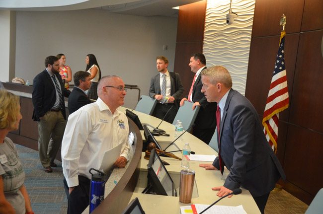 Bunnell City Commissioner John Sowell, left, speaking with Rep. Paul Renner after the legislative delegation meeting at Palm Coast City Hall, while Sen. Travis Hutson, further back, speaks with School Board Chairman Trevor Tucker. (© FlaglerLive)