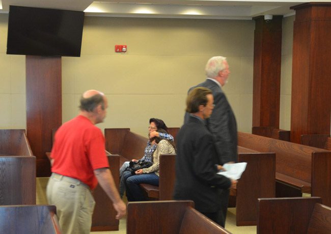 Jonathan Canales, holding the document, walking out of the courtroom last week after a hearing as the mother of the victim in the case shields Tiffany Norman against her so she is not able to see the man she says shot her in the neck four years ago in their Mondex home. It was the first time the two had been in the same room again since the shooting. (© FlaglerLive)