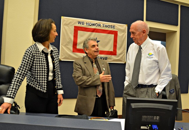 Commissioner Charlie Ericksen, right, being welcomed back this morning by colleagues Barbara Revels and George Hanns. (© FlaglerLive)