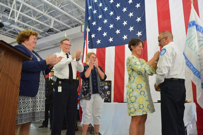 Lisa Forete pins her husband Jerry Forte's Chief badge as he took over the Palm Coast Fire Department's leadership this afternoon, from the retiring Mike Beadle, left, whoi was flanked by his wife Deedee to the right and Deputy City Clerk Kate Settle. (© FlaglerLive)