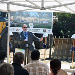 Ivan Cosimi, for a dozen years the CEO at SMA Healthcare, speaking to a crowd of several dozens at Tuesday's groundbreakling. A rendering of the facility is behind him. (© FlaglerLive)