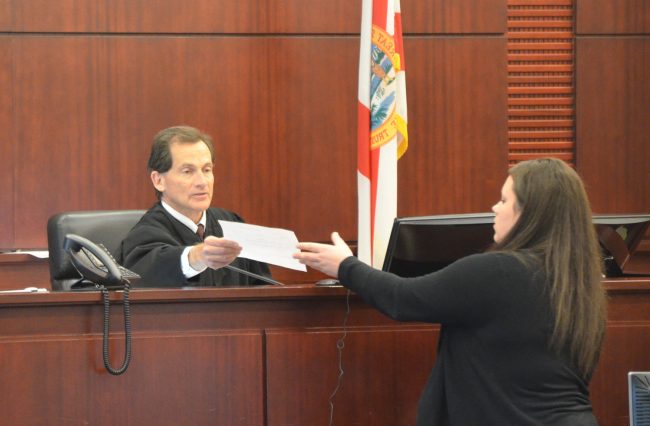 Circuit Judge Dennis Craig hands over the jury verdict form to the clerk to be read. An older woman, a member of C.J. Nelson's family, during a lull in the trial had called out to the judge from the audience, telling him he was doing a great job. The judge smiled and urged the woman to be quiet, as all proceedings are recorded. Click on the image for larger view. She thanked him again when court adjourned. (© FlaglerLive)