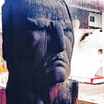 The face of Crazy Horse carved in 1952 out of Ponderosa Pine by Korczak Ziolkowski. The white sculpture visible through the rain-streaked window pane is a scale model of the mountain sculpture of Crazy Horse.