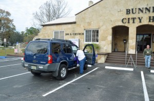 Commissioner Daisy Henry, who operated her own shuttle service to the polls, helps a voter out of her car. Click on the image for larger view. (© FlaglerLive)