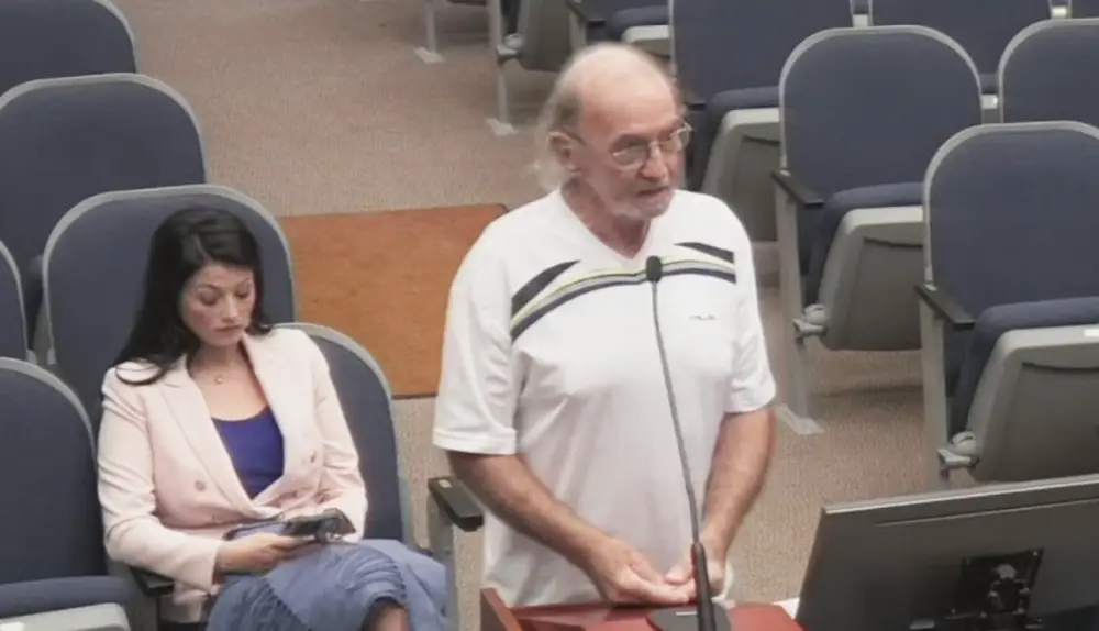 Jeff Davies, the now former member of the Contractor Review Board, addressing the County Commission about his qualifications, with Heather Haywood, a member of the county's planning board, seated. (© FlaglerLive via Flagler County TV)