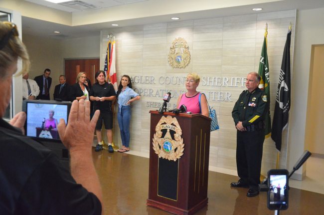 Renée Deangelis, mother of Savannah, 23, who died of an overdose last fall, speaks to the press this afternoon, with her husband, Charles, and her daughter Christina, to the left of the image, and Sheriff Rick Staly to the right. Assistant State Prosecutor Jason Lewis and State Attorney R.J. Larizza are toward the left corner. Click on the image for larger view. (© FlaglerLive)