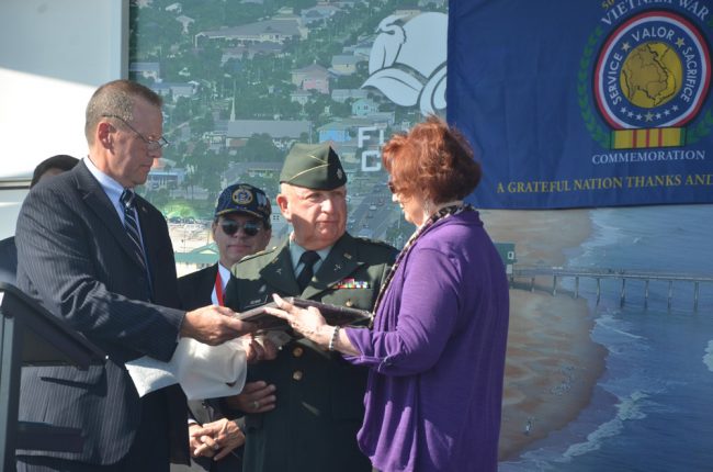 Lt. Col. Harry W. Gilman (ret.), center, accepting the Flagler County Veterans of the Year award from David Lydon and Gary E. Dekay's widow. Click on the image for larger view. (© FlaglerLive)