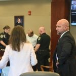 Defense attorney Aaron Delgado, right, speaks with Assistant State Attorney Melissa Clark as Delgado's client, Melvin Adona, is being finger-printed after his sentence to 10 years in prison, in a hearing that should not have ended when it did: Delgado and Clark moments later spoke with Circuit Judge Dawn NIchols in chambers to let her know she had forgotten to hear their closing arguments. The case is on appeal on that basis. (© FlaglerLive)