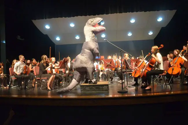 Look who turned up at the Flagler Youth Orchestra's last concert of the season at the Flagler Auditorium Wednesday evening: Conductor Joe Corporon donned a dinosaur suit to conduct the theme from 'Jurassic Park,' one of two dozen pieces performed by four orchestras, from relative beginners to well advanced students. The concert also featured a farewell to 12 graduating seniors, each of whom received a $200 college scholarship from the orchestra. Superintendent Jim Tager, School Board member Maria Barbosa and Sheriff Rick Staly were among the audience, a near full house. (© FlaglerLive)
