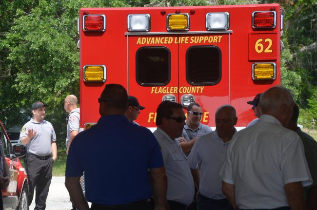 Flagler County Fire Chief Don Petito, center, with county commissioners, Bunnell citry commissioners and others marking the ceremonial transfer of Bunnell's fire station to the county, in the shadow of a new, eighth rescue unit that will be operating out of the station, to the benefit of the entire county. (© FlaglerLive)