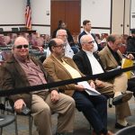 Council candidate Jeanie Duarte, in the red shirt, eyes members of the Palm Coast Charter Review Committee at a February 24 workshop from which she was not thrown out. Tony Amaral, a candidate in the same district, is third from left in the background. (© FlaglerLive)