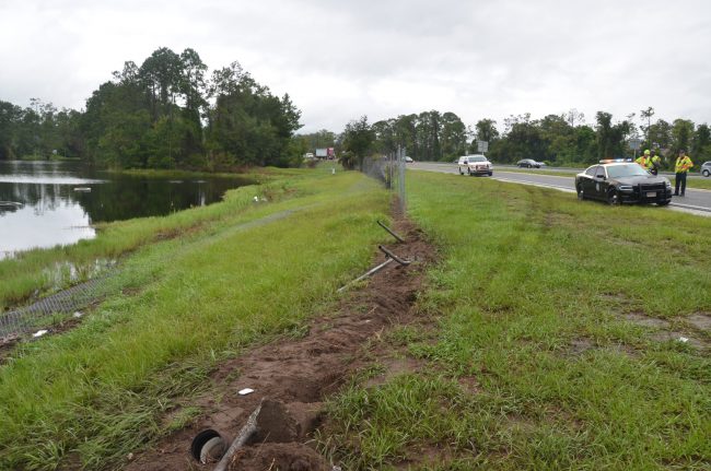 The tire marks in the grass trace the way the Malibu veered off the exit ramp, crashed through the fence and flipped into the pond. Click on the image for larger view. (© FlaglerLive)