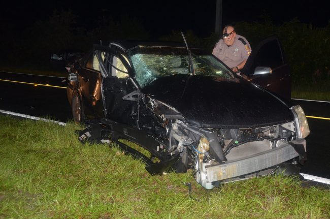 Florida Highway Patrol Traffic Homicide investigator Pete Young examining the Cadillac, which took the brunt of the collision on its passenger side. Click on the image for larger view. (© FlaglerLive)