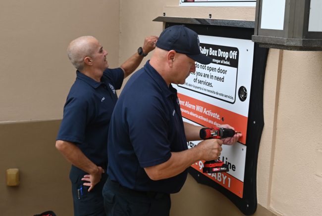 The Palm Coast Fire Department's Lt. Joey Paci, left,  and Lt. Matt Stevens, adding the finishing touches on the outside portion of the baby box this afternoon, just before the blessing. (© FlaglerLive)