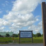 The site set aside for the hoped-for south-0side library, opposite a sign announcing the new Sheriff's Operations Center, which is well under construction. Only weeds are growing behind the library sign. (© FlaglerLive)