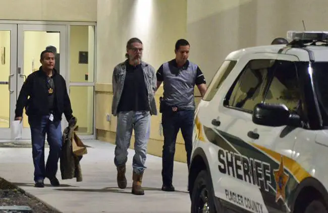 Michael Cummings being led out to a patrol car, on his way to the county jail this evening, flanked by detectives Mark Moy, left, and Jorge Fuentes, who worked the case. (© FlaglerLive)