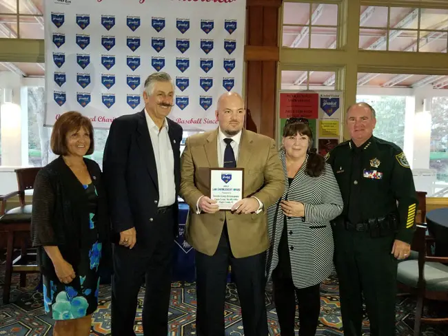 Flagler County Sheriff Detective George Hristakopoulos, center, accepting the Greatest Save award Monday from baseball legend Rollie Fingers, the tallest man in the room. With them were Director Nancy Sebastian, Hristakopoulos's mother, and Sheriff Rick Staly. (FCSO)