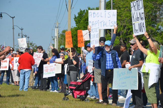 More than 100 people stretched across Palm Coast Parkway on both sides of Boulder Rock Drive this morning between 10 a.m., and noon. Many demonstrators went on to other planned marches in the region, from St. Augustine to Orlando. Click on the image for larger view. (© FlaglerLive)