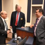 Thursday night trinity at the Flagler County Commission. From left, County Attorney Al Hadeed, who is retiring in a few days, Commissioner Greg Hansen, and newly chosen County Attorney Michael Rodriguez, moments after the commission's 5-0 vote in his favor. (© FlaglerLive)