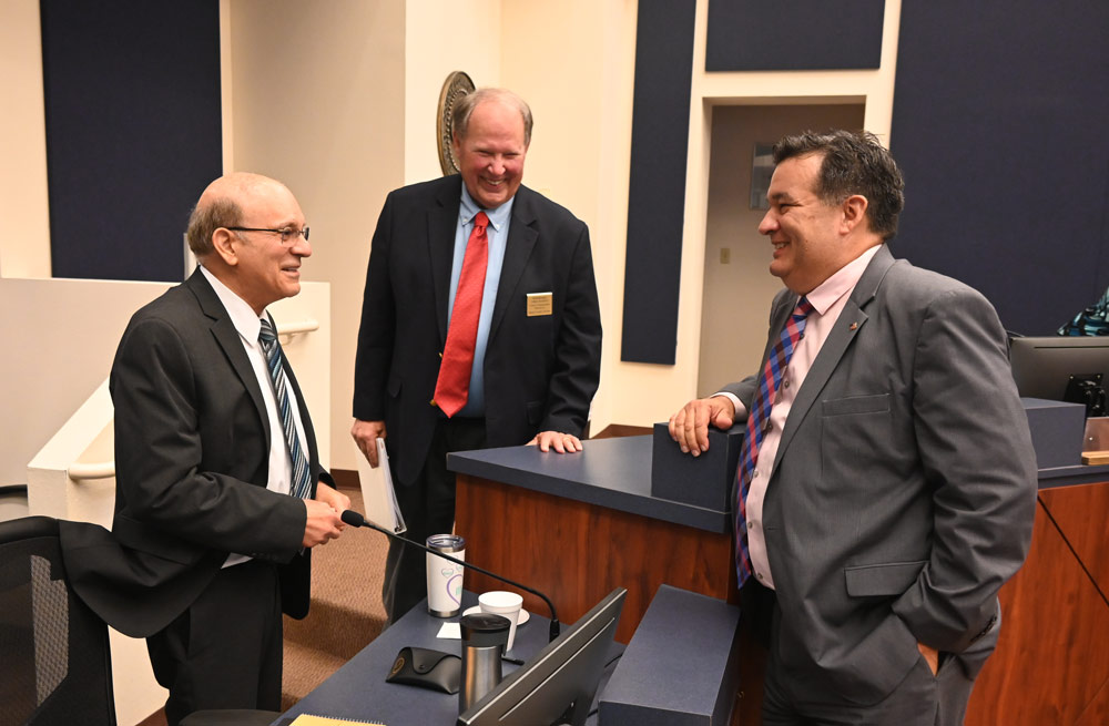 Thursday night trinity at the Flagler County Commission. From left, County Attorney Al Hadeed, who is retiring in a few days, Commissioner Greg Hansen, and newly chosen County Attorney Michael Rodriguez, moments after the commission's 5-0 vote in his favor. (© FlaglerLive)