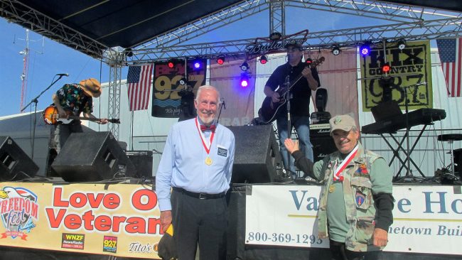 Still-Commissioner George Hanns, later in the day, with fellow-Commissioners Charlie Ericksen and, on stage at the guitar, Nate McLaughlin. Click on the image for larger view. (George Hanns)