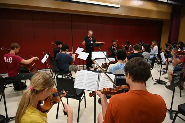 From left in the foreground, Cellist Joseph Fisk and violinists Noemi Malinowski, and Russell Bader with the Harmony Chamber Orchestra in rehearsal. (© FlaglerLive)