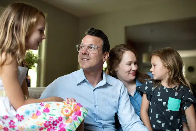 Drew Calver sits with his wife, Erin, and daughters Eleanor (left) and Emory (middle) in their Austin, Texas, home where he had a heart attack on April 2, 2017. Calver, a high school teacher, has health insurance through his school district, but still faced a $108,951.31 bill. (Callie Richmond for KHN)