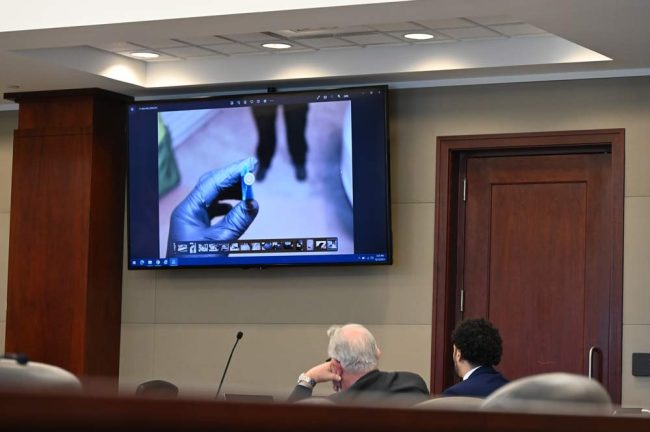 Brenan Hill, right, looks at one of the images shown the jury today, this one of one of three shell casings recovered after the shooting. (© FlaglerLive)
