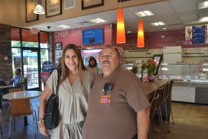 Palm Coast Mayor Milissa Holland and Dunkin Donuts Lotto Club member Joe Vece, standing in front of the table built especially for the 20-member club, which has been meeting at the restaurant every day for over a decade. Click on the image for larger view. (© FlaglerLive)