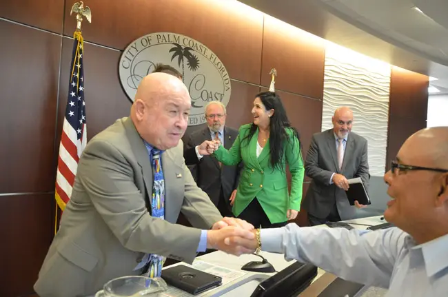 Newly-minted Palm Coast Council member Jack Howell, in the foreground, is congratulated by a supporter as Mayor Milissa Holland fist-bumps fellow-councilman and now-Vice Mayor Nick Klufas (behind Howell), with Councilman Bob Cuff and, to the right, Eddie Branquinho, who was also sworn-in today. (© FlaglerLive)