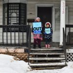 Children hold signs on the porch of a house as protesters march in Minneapolis against Immigration and Customs Enforcement on Jan. 10, 2026.