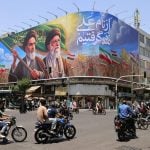 People ride motorcycles past a large billboard in central Tehran on June 8, 2026.