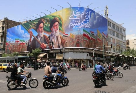 People ride motorcycles past a large billboard in central Tehran on June 8, 2026.