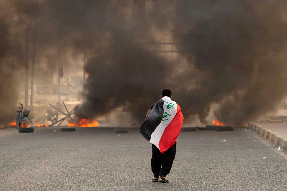 An Iraqi person walks down a road blocked by burning tires in Basra in August 2002. 