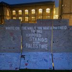 Visible in this image is an artist's recreation of the West Bank apartheid wall which guests of the encampment are invited to draw on. In the background are buildings belonging to Reuben College and the Bodleian Library's Radcliffe Science Library.