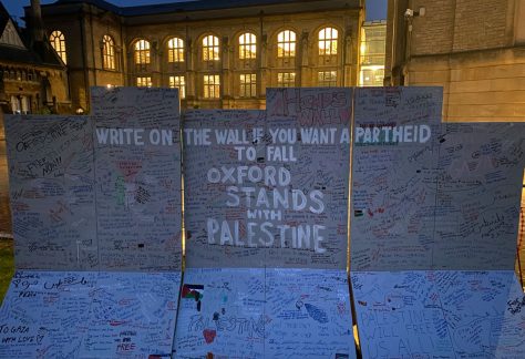 Visible in this image is an artist's recreation of the West Bank apartheid wall which guests of the encampment are invited to draw on. In the background are buildings belonging to Reuben College and the Bodleian Library's Radcliffe Science Library.