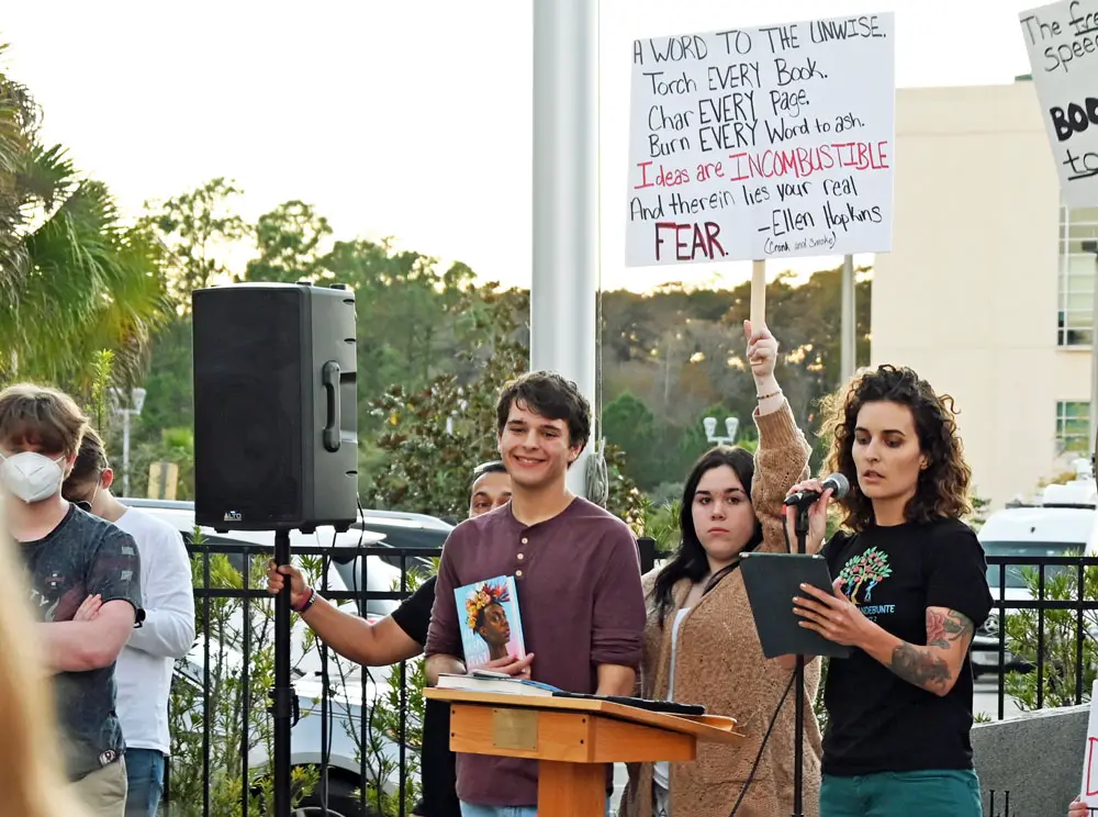 Jack Petocz, center, holding a copy of <i>All Boys Aren't Blue</i>, at the protest he organized against book bans by the school district last November. Next to him is Flagler Palm Coast High School student Alysa Vidal, holding the sign Petocz made and was featured holding in one of the New York Times' pictures, and School Board member candidate Courtney VandeBunte. (© FlaglerLive)