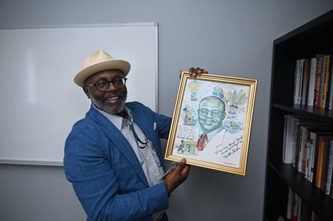 City Manager Alvin Jackson in his office at the new City Hall, with an artist's rendering of himself at a previous point in his career. (© FlaglerLive)