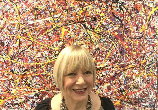 Jan Jackson, curator of Grand Gallery, poses beside “Vertigo,” a work by Dennis Mialki that is part of the current exhibit, “Elements III, Part 2.” (© FlaglerLive)