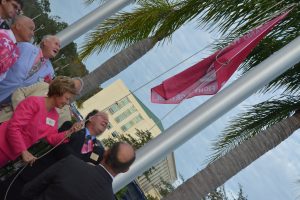 Tax Collector Suzanne Johnston raises the Pink Army Flag amid a platoon of men. (c FlaglerLive)