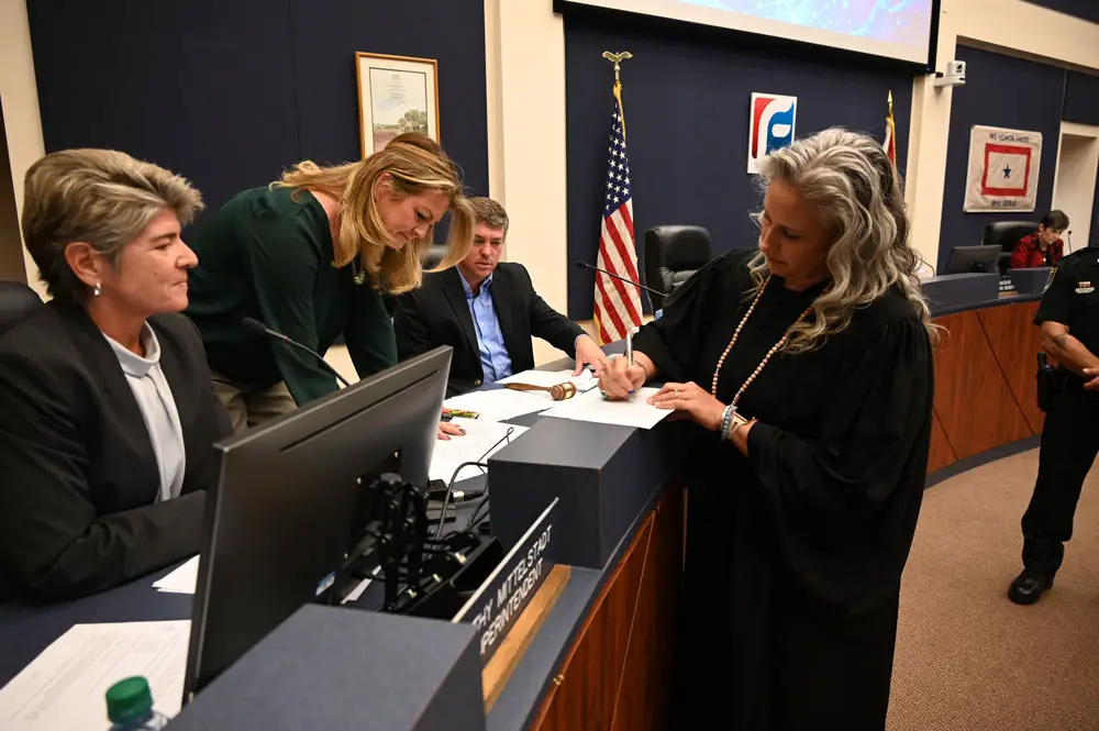 County Judge Melissa Distler, right, signing papers ratifying the elections of Trevor Tucker, center, Chairman of the School Board, and Colleen Conklin, second from left, vice chair. Superintendent Cathy Mittelstadt is to the left. (© FlaglerLive)