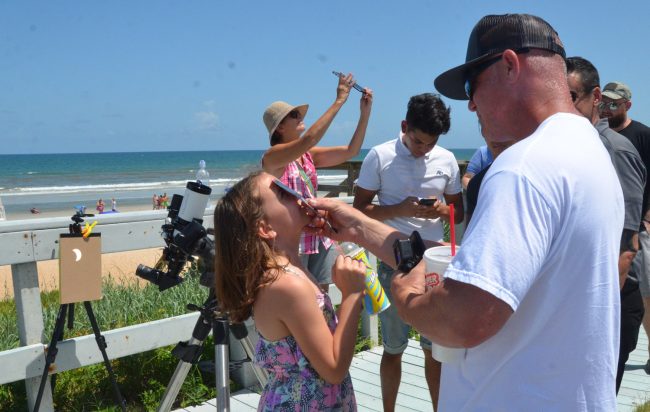 Daniel Craft pulled his daughter Kiley out of school to experience the eclipse, which she was looking at as it was about halfway to its peak, as its refraction to the left indicated. Click on the image for larger view. (© FlaglerLive)