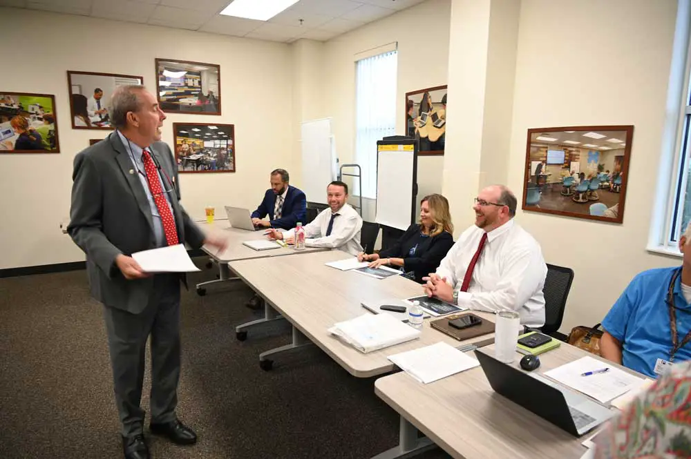 Three smiling lawyers and a mayor: Palm Coast Mayor David Alfin, standing, liked seeing the smiles on the faces of Assistant County Attorney Sean Moylan, seated, second from left, Palm Coast City Attorney Neysa Borkert, and Chris Wilson, the attorney representing the Flagler County School Board on concurrency issues. (© FlaglerLive)